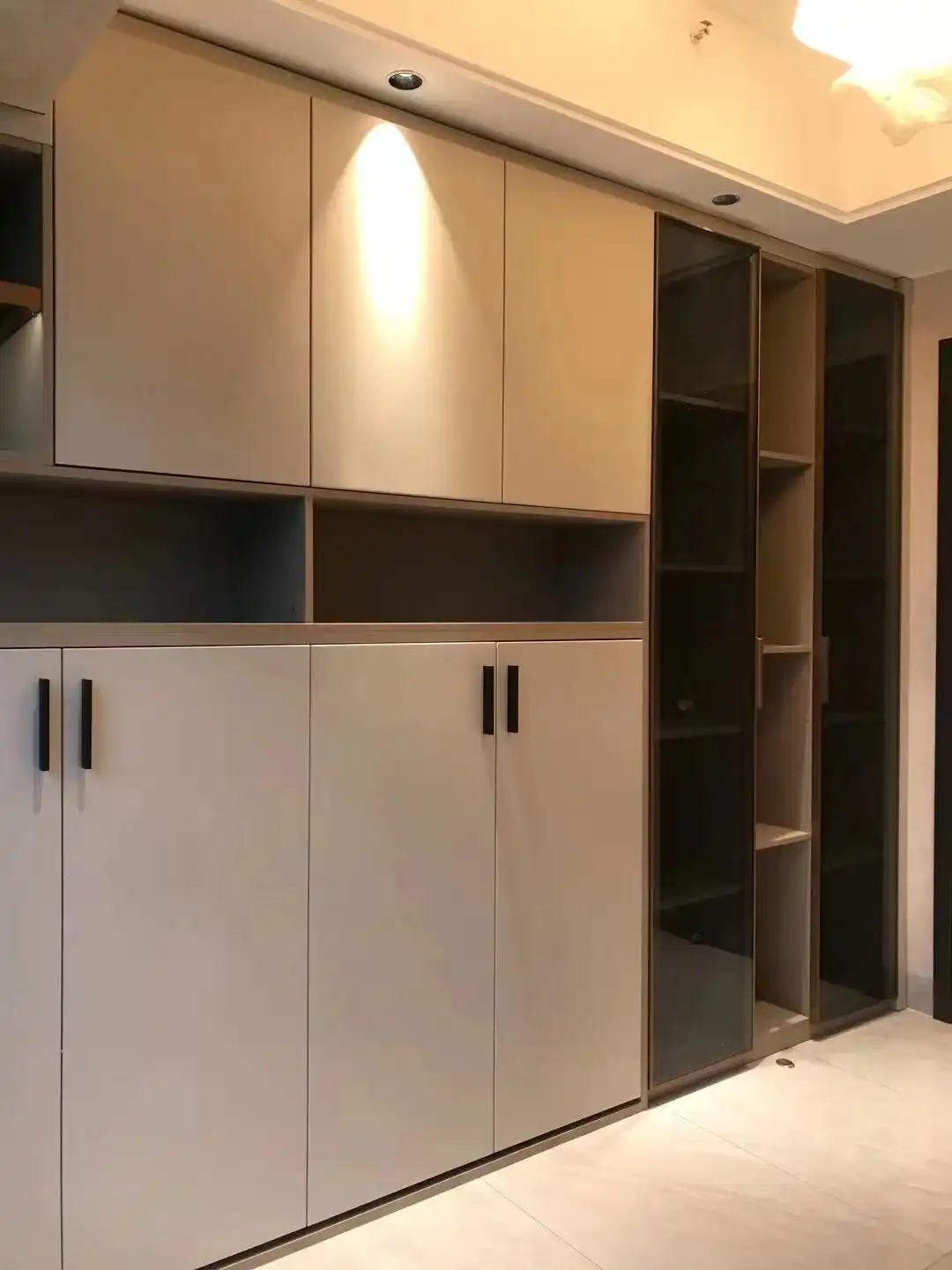 Hotel room storage design with light wood cabinetry, glass doors, and recessed ceiling lighting
