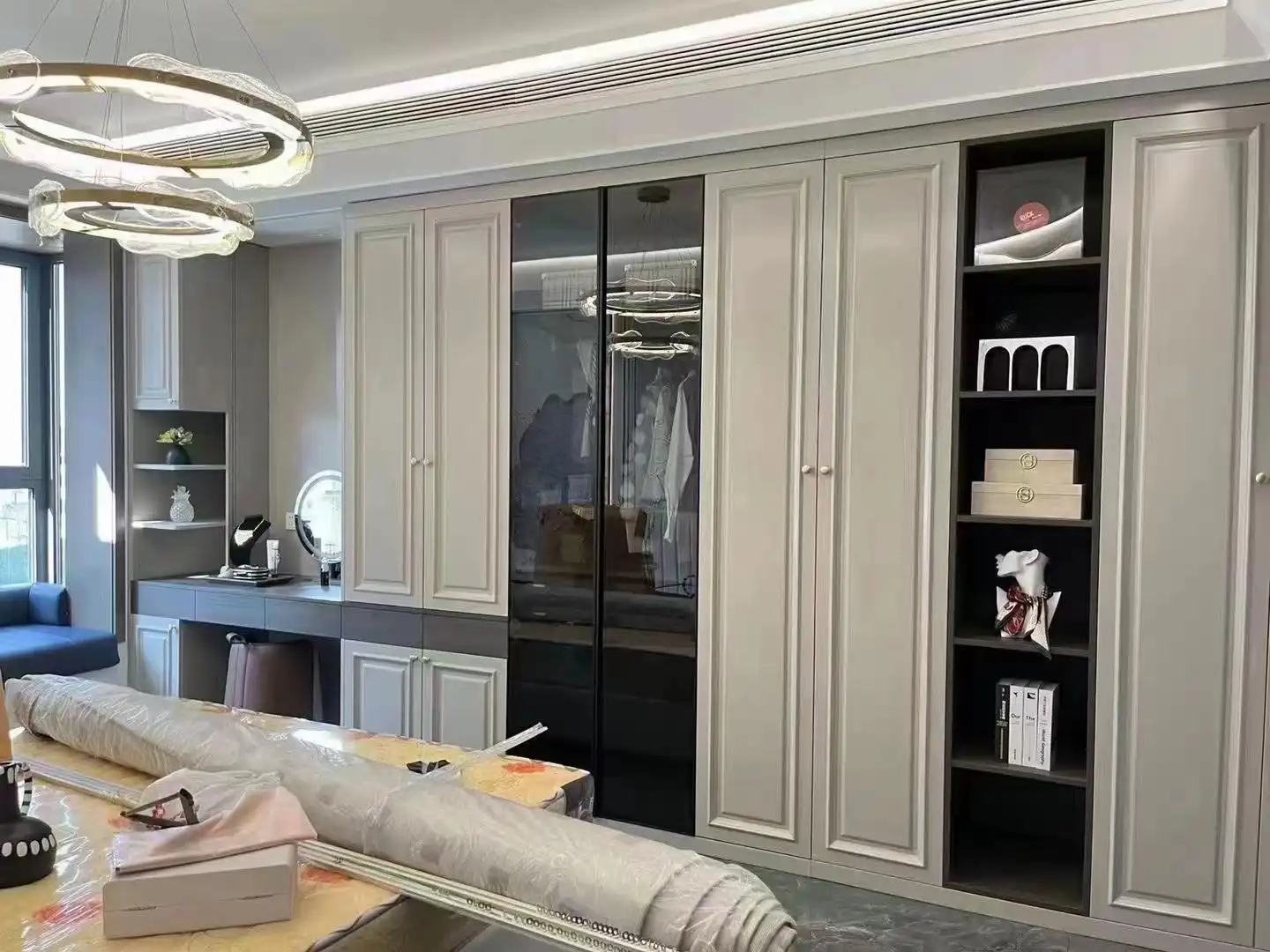Contemporary master bedroom design with gray wardrobe, glass door cabinets, and circular chandelier