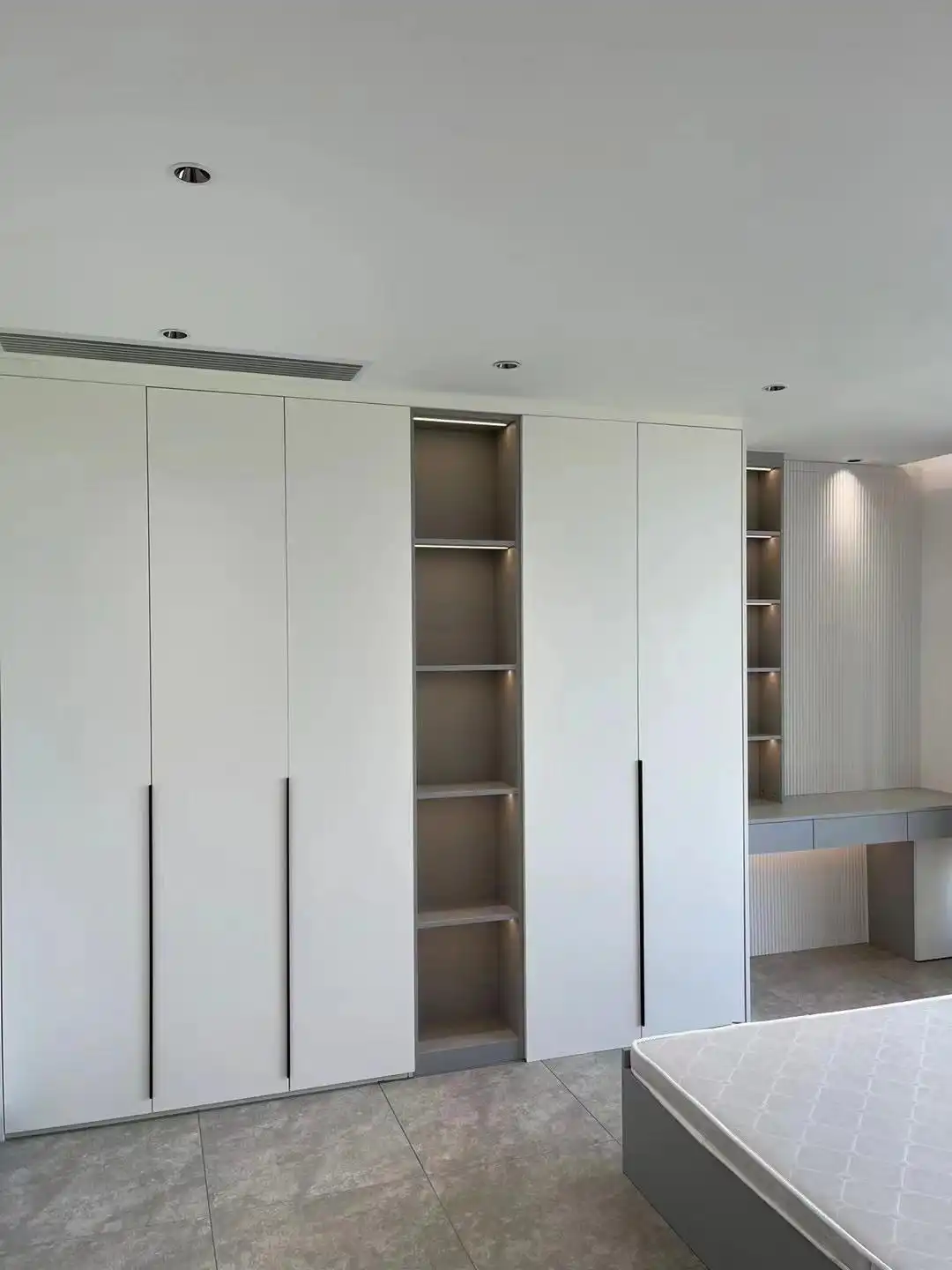 Modern master bedroom design with white wardrobe, LED-lit open shelves, and built-in desk area