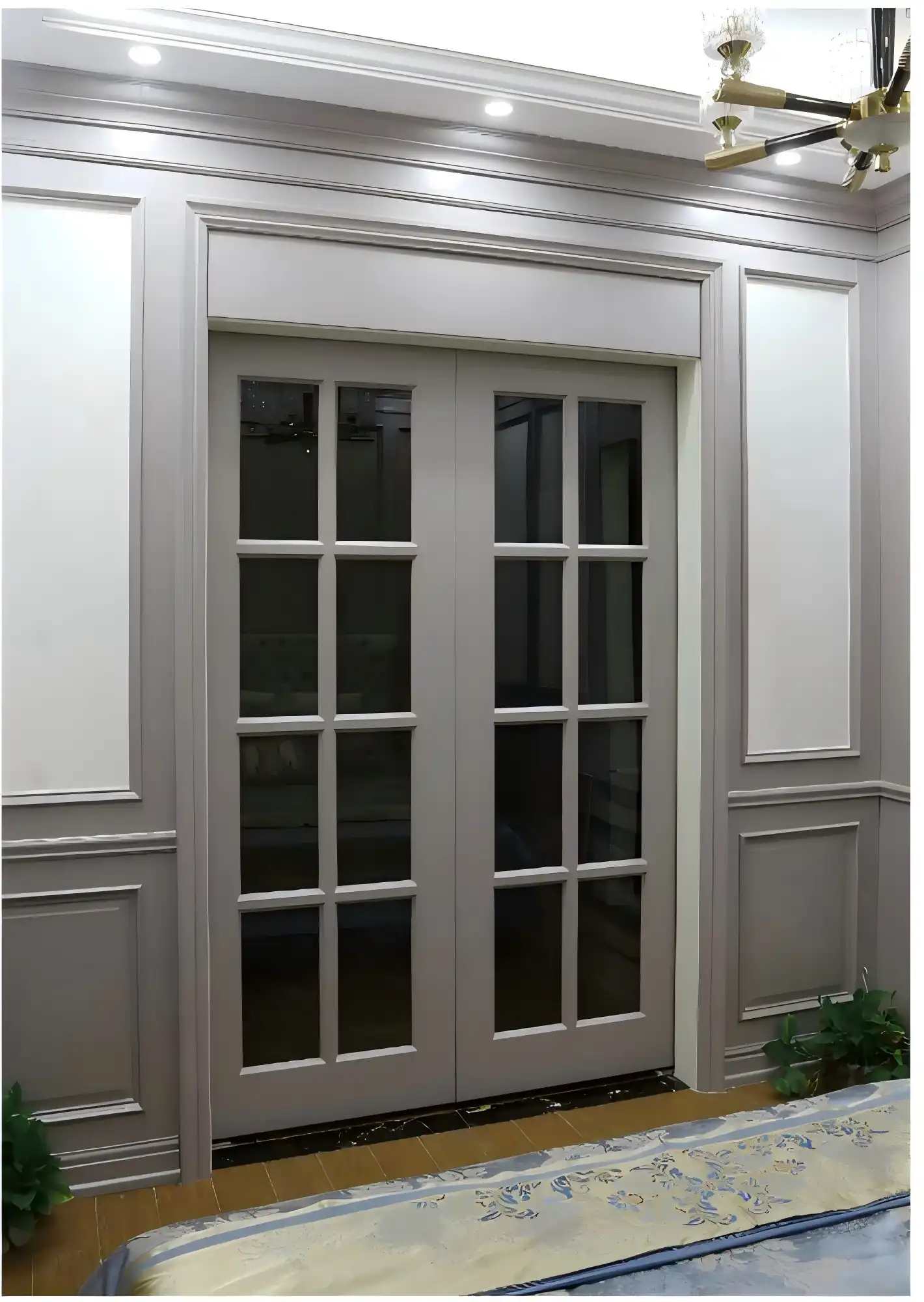 These elegant interior French doors feature a modern gray finish with multi-pane glass panels and clean black grid lines, creating a sophisticated contemporary aesthetic. The floor-to-ceiling configuration maximizes natural light, while the seamless integration with wall paneling enhances the cohesive look. This design demonstrates how contemporary French doors can serve as both functional barriers and striking design elements, perfectly complementing the ornate ceiling details and overall sophisticated interior.