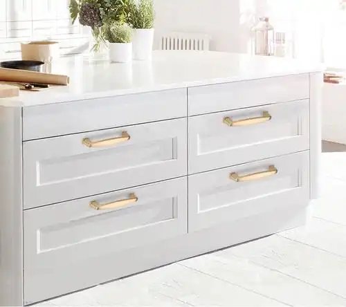 White kitchen island with gold handle hardware, four drawers, and potted green plants on countertop.