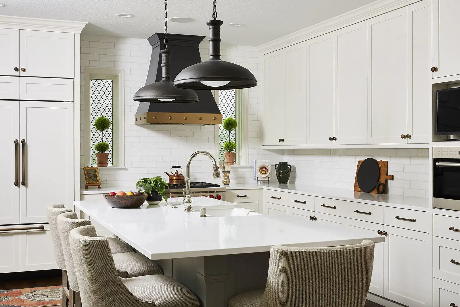 Traditional white kitchen with black metal pendant lights, marble countertop island, brass hardware, and brick backsplash