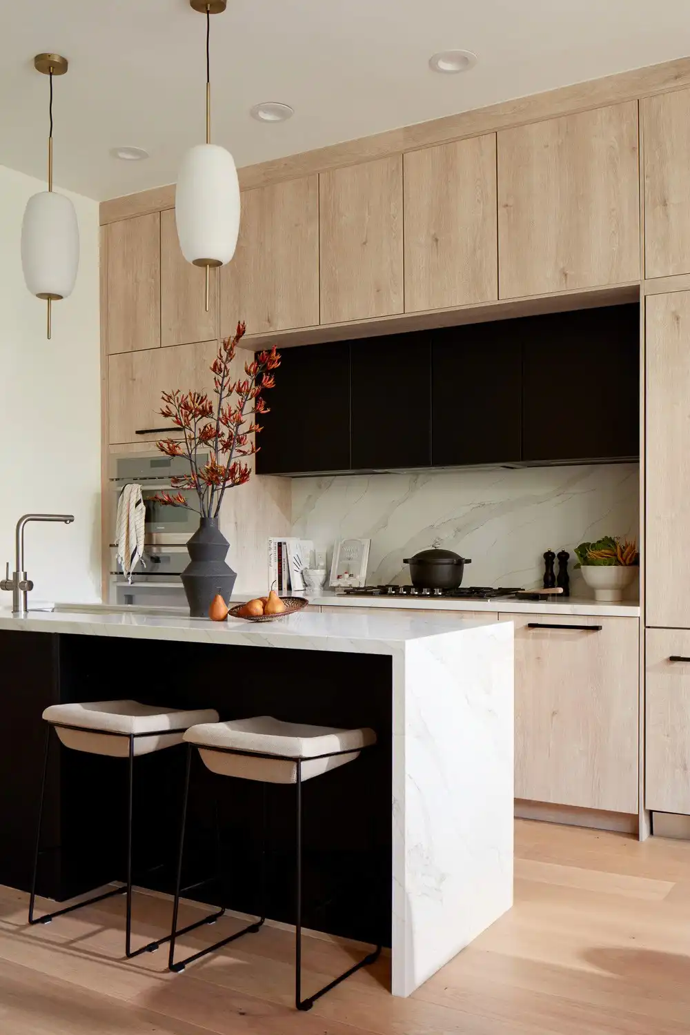 Contemporary kitchen with light wood and black cabinetry, marble countertop island, white pendant lighting, and wooden flooring