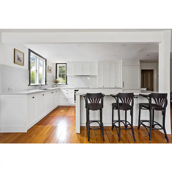 Clean White Shaker-Style Kitchen Cabinets with Quartz Countertops, Contrasting Dark Black Bar Stools, and Warm Wood Flooring.