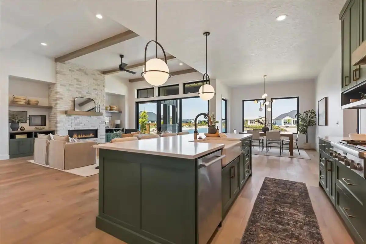 Open Concept Kitchen with Trendy Deep Green Shaker-Style Cabinets, a Large Island with a White Countertop, and Natural Wood Flooring, adjacent to a living room with a stone fireplace.