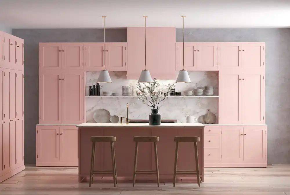 Bold modern kitchen featuring light blush pink Shaker cabinets covering the walls, a white marble backsplash, and a pink island with wooden barstools.
