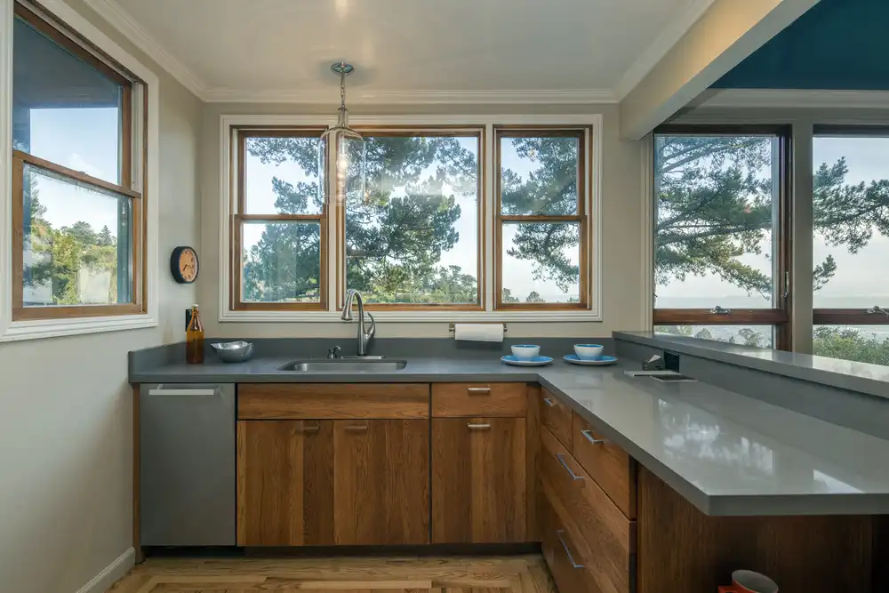 U-shaped kitchen with light aqua blue traditional-style cabinets, featuring raised panel doors, glass inserts on the upper cabinets, and a black range hood against a white tiled wall.