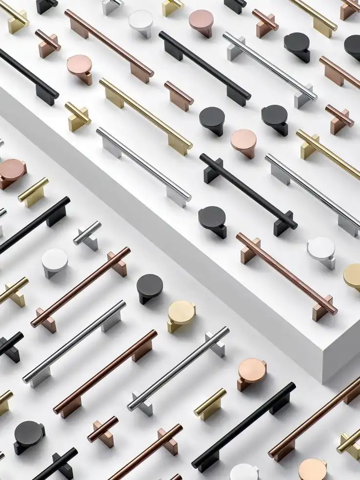 A flat-lay display of high-quality kitchen cabinet hardware, featuring modern T-bar pulls and round knobs in various finishes including matte black, brushed gold, satin nickel, and rose copper.