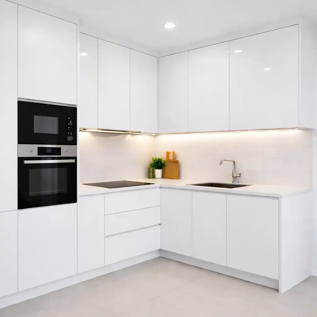 A clean L-shaped small kitchen cabinet layouts with flat-panel white doors, integrated microwave and oven, an induction cooktop, and warm LED under-cabinet task lighting.